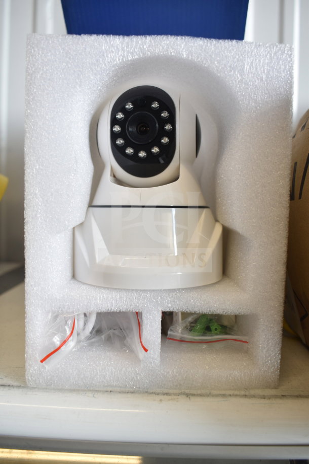 Wi-Fi video surveillance camera in original box, shows lens and infrared LEDs, includes cables and accessories.