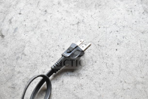 A black power cord with a two-prong plug on a gray surface, part of a Nostalgia countertop griddle, 115 volts, 1 phase.