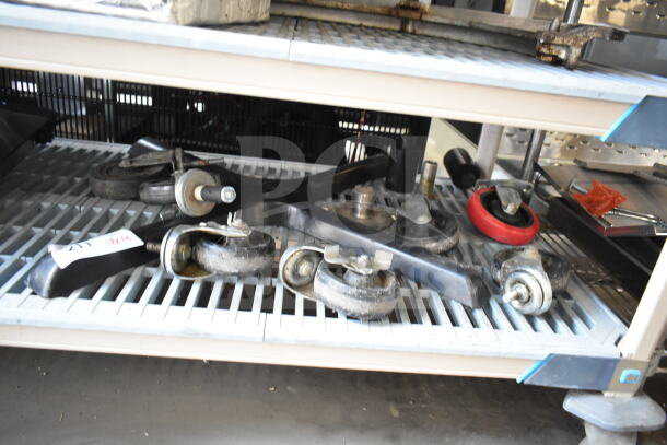 Various items including commercial casters and a table base piece on a metal shelf, items are in used condition.