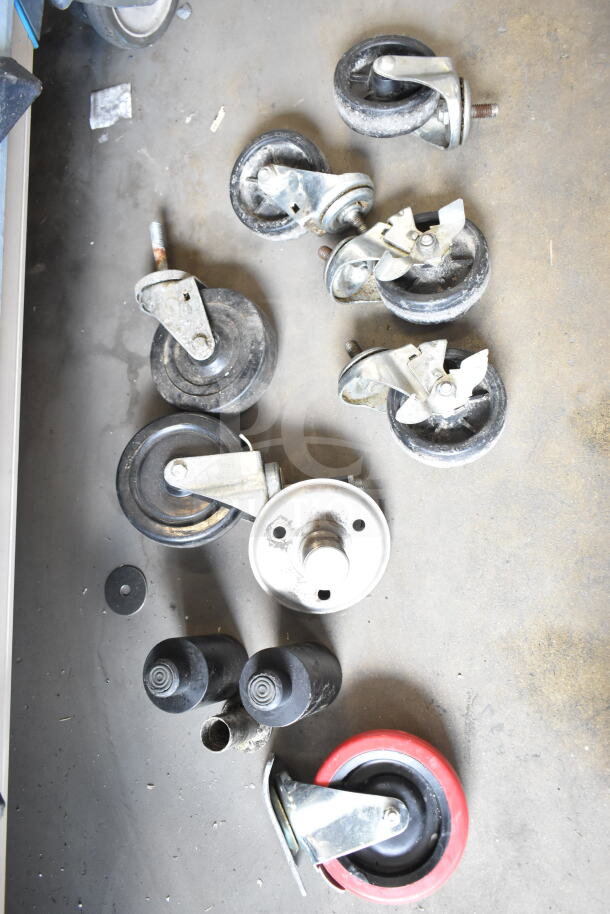 Various commercial casters and a table base piece in used condition, featuring metal and rubber components, some rust visible.