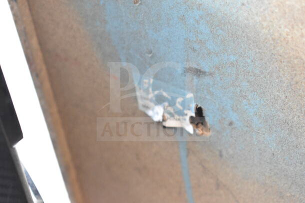 Close-up of a damaged and peeling blue label on a textured surface. Condition indicates wear and deterioration.