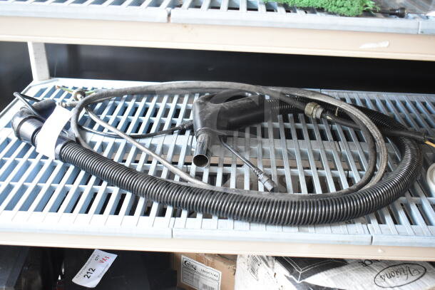 Vacuum hose attachment with black handle, coiled hose, and various connectors in good condition on wire shelf.