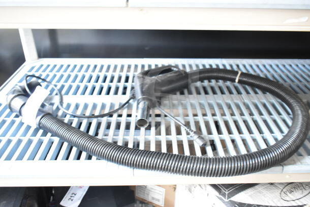 Vacuum hose attachment, black, flexible, in used condition, coiled on a metal shelf. No visible brand markings.