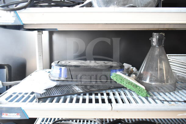 Assorted items including an espresso bean grinder hopper, slushie machine hopper lid, and dustpan broom on a shelf.