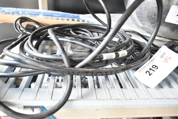 Coiled black cords on a gray slatted surface, tag with "219" and "6X" visible. Some cords have attached labels.