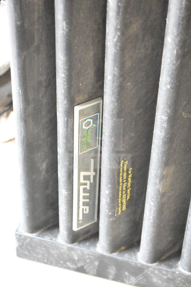 True cooler kickplate, black metal, embossed logo, natural refrigerant label, good condition, visible cleaning instructions.