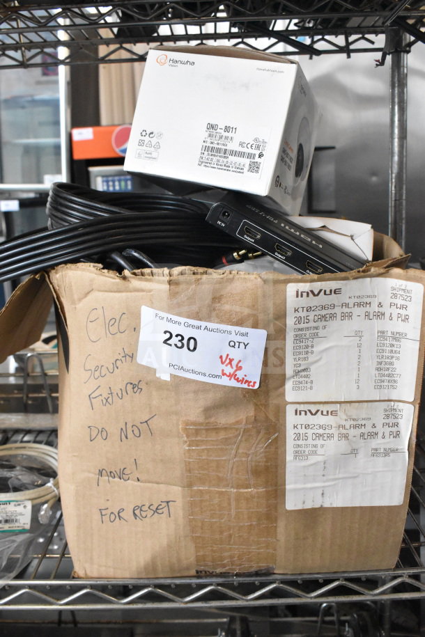 Box containing various items including an Hanhwa Vision QND-8011 box, HDMI splitter, and cables. Labels indicate auction details and contents.