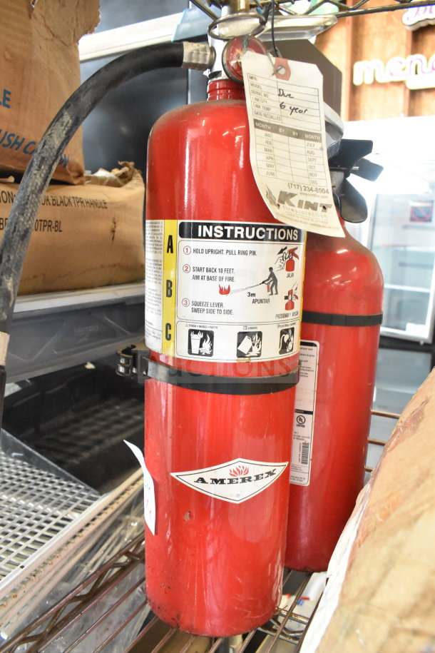Two red fire extinguishers, including Amerex brand, with instruction labels and inspection tags visible. Buyer pick-up required.