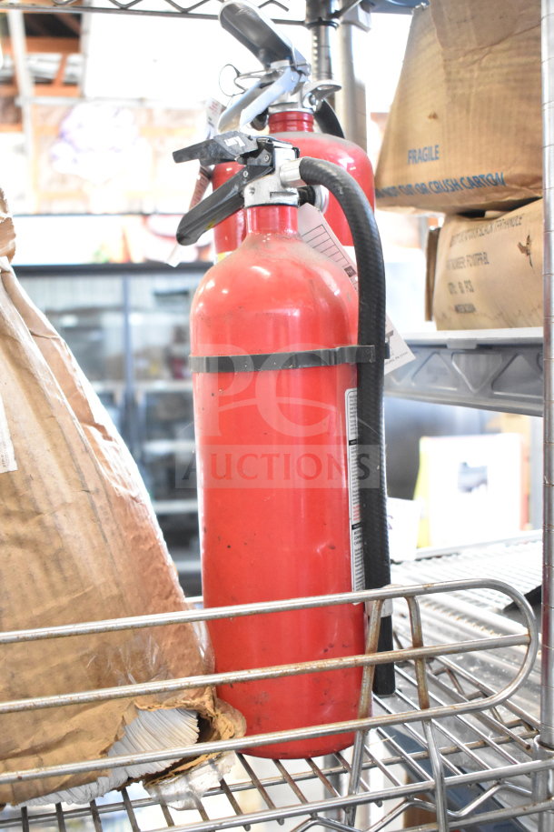 Two red fire extinguishers, including Amerex, on a metal shelf. Visible wear. Pickup only, no shipping.