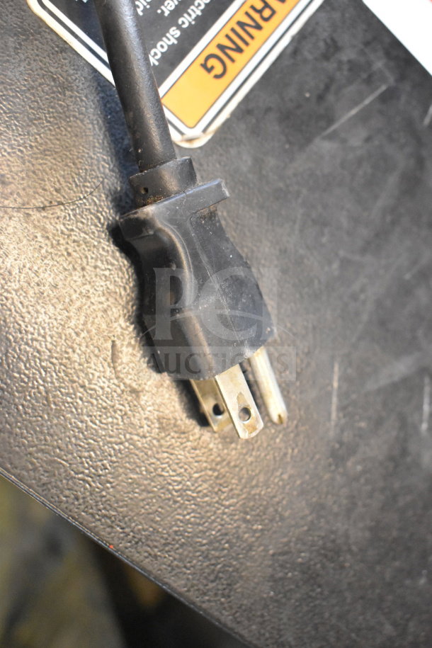 A black power cord with a standard three-prong plug is shown. An orange "WARNING" label is partially visible nearby.