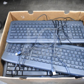 Box of multiple black computer keyboards with USB connectors, various models, stacked in used condition.