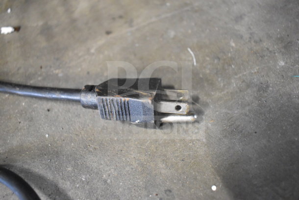 Aged black power plug on concrete surface, showing signs of wear. Part of a light fixture for auction.