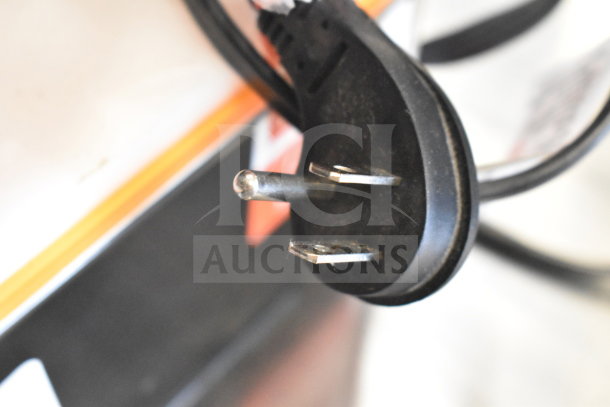 Close-up of a two-prong power plug attached to a JBL Partybox 110 speaker display. Black cable, orange trim.