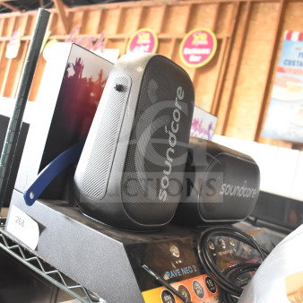 Soundcore speaker on store display, model Rave Neo 2. Black oval design, visible branding, includes interactive labels.
