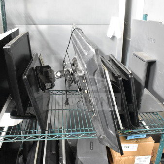 Eight monitors on a shelf, brands include Toshiba, HP, and Onn; various conditions. Tags indicate auction lot details.