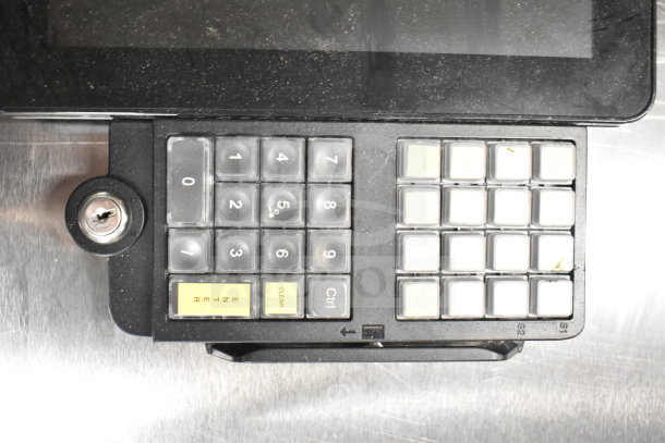 Keyboard and lock panel attached to a monitor, featuring numeric and function keys, with notable wear and smudging.