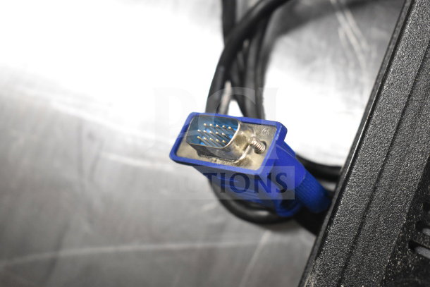 Close-up of a blue VGA cable connector, part of a lot including 8 various monitors by Toshiba, HP, and Onn.