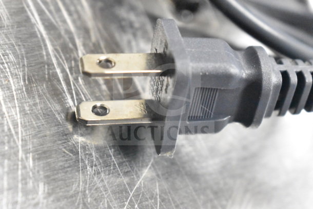 Close-up of a black electrical plug on a textured surface. No monitors visible.