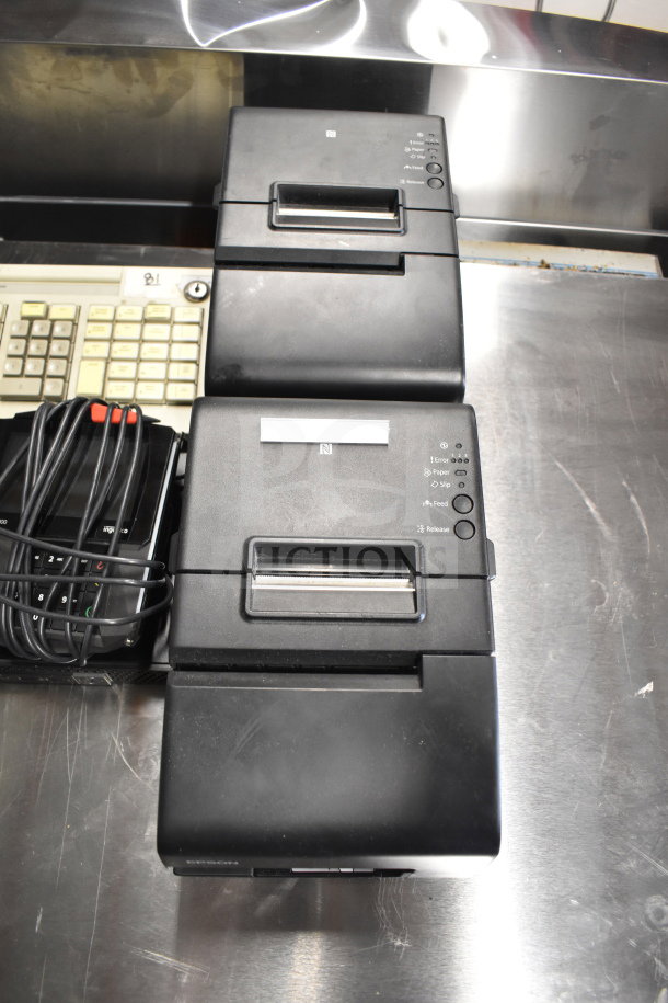 Stack of two black receipt printers on a stainless steel surface, with a coiled power cord nearby.
