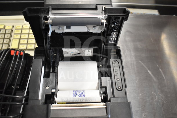 Open receipt printer showing paper roll, part of a lot including Toshiba monitors and office telephone.