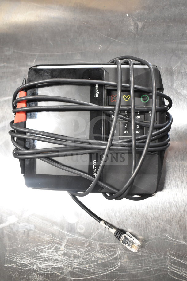 Ingenico Lane/7000 payment terminal with wrapped cord on metal surface. Marks visible, check condition. Part of auction lot.