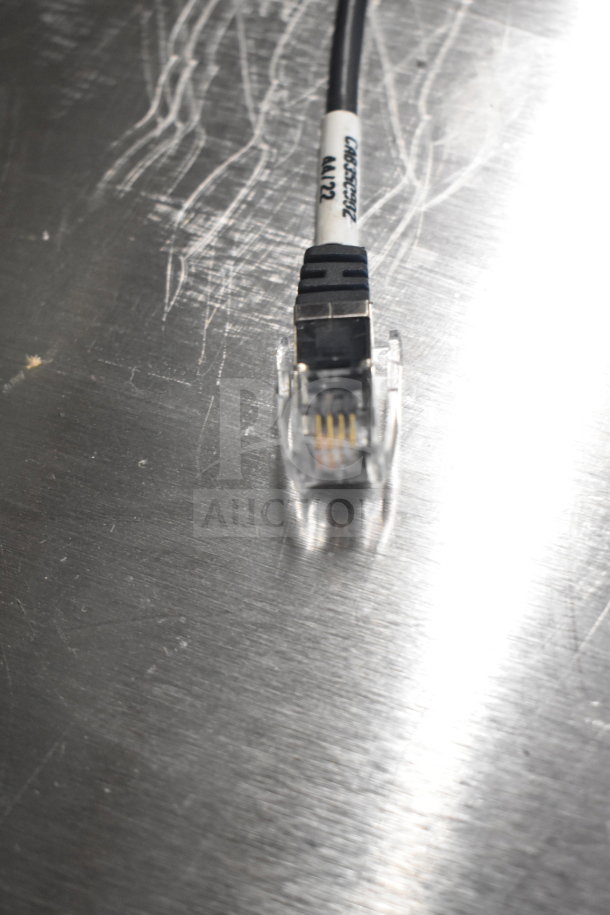 Close-up of an Ethernet cable with labeling, part of a bulk auction lot featuring Toshiba monitors, a corded office phone, and receipt printers.