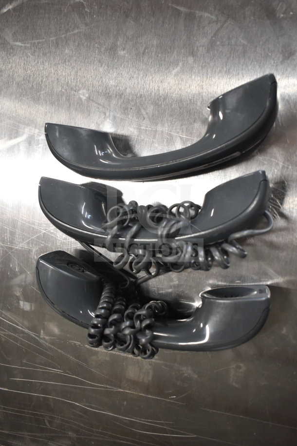 Three black corded telephone handsets with coiled cords on a reflective surface; slightly used condition.