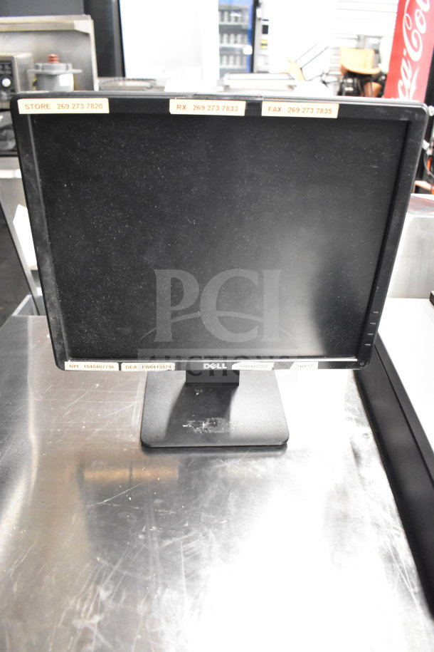 Dell monitor with labels including contact numbers, set on a metallic countertop. Condition shows signs of wear.