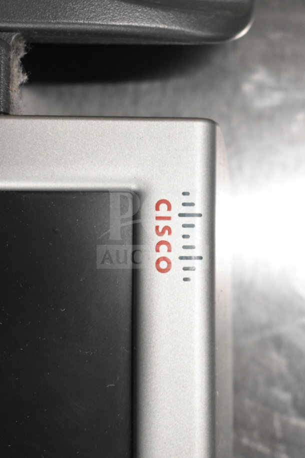 Close-up of a Cisco device, silver and black, featuring the Cisco logo on a metallic frame. Condition appears used.