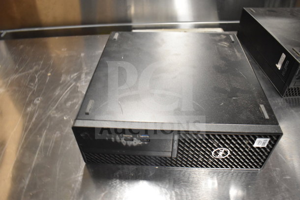 Dell computer tower on a metal surface, shows front USB and audio ports. Labels indicate model and service tags. Dust visible.