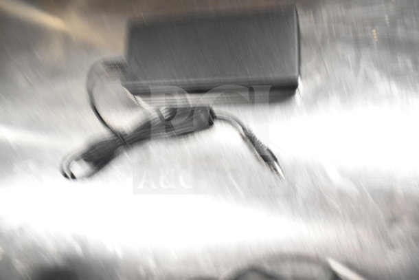 Blurry image showing miscellaneous electronic items, possibly including power adapters or cables, unclear condition.