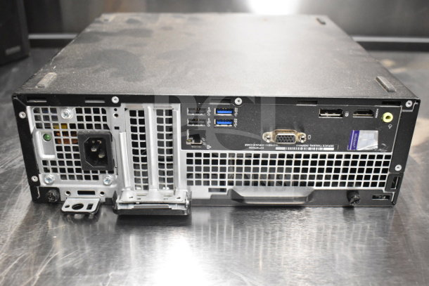 Rear view of a Dell computer tower showing various ports, slightly dusty, part of a lot with office phones and card reader.