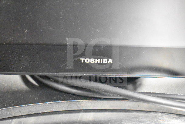 Toshiba computer monitor, close-up view, showing brand logo. Dust visible on the surface. Wires slightly visible below.