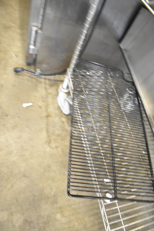 Two-tier metal storage rack with wires, on wheels. Includes drop-in bins. Industrial kitchen setting, used condition.