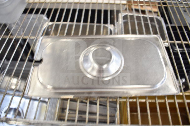 Two-tier metal wire shelving with various metal drop-in bins, featuring a stainless steel lid. Items appear in used condition.