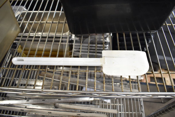 Two-tier lot with assorted items on metal shelves, including a white plastic spatula and plastic bins. Items show moderate wear.