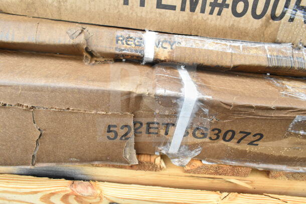 Stack of brand new scratch and dent items in boxes, including Regency branded work table and pan rack, some packaging damage.