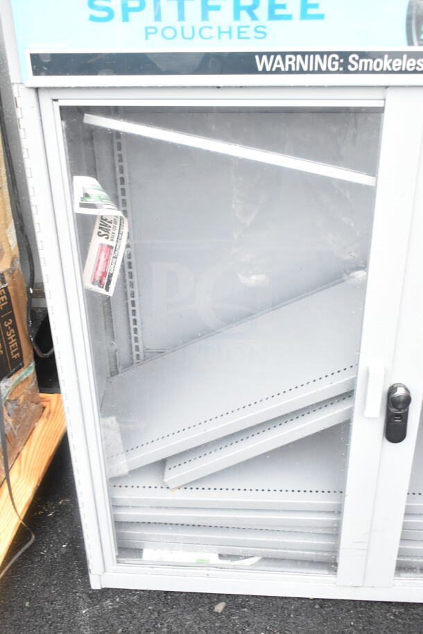 Gray metal 2-door display cabinet merchandiser with glass front. Visible shelves askew, door handle intact, some wear.