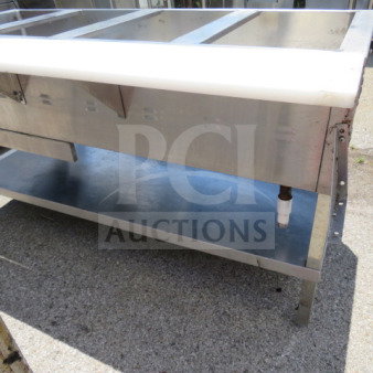Four-well steam table with cutting board, under shelf, stainless steel, minor wear, perfect for food service use.