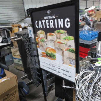 Black metal sign frame, 22.5x25x61 inches, featuring Wayback Catering promotional poster. Used condition, visible in cluttered room.