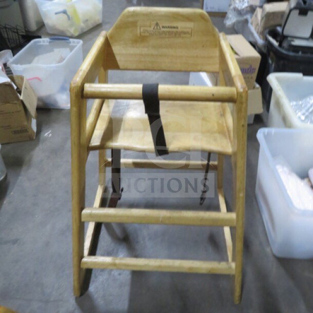 Wooden high chair with safety straps, natural finish, visible wear, and warning label on the backrest.