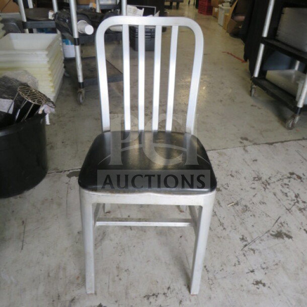 Aluminum chair with black cushioned seat, model 2XBID. Features a slatted backrest; good condition, suitable for indoor use.