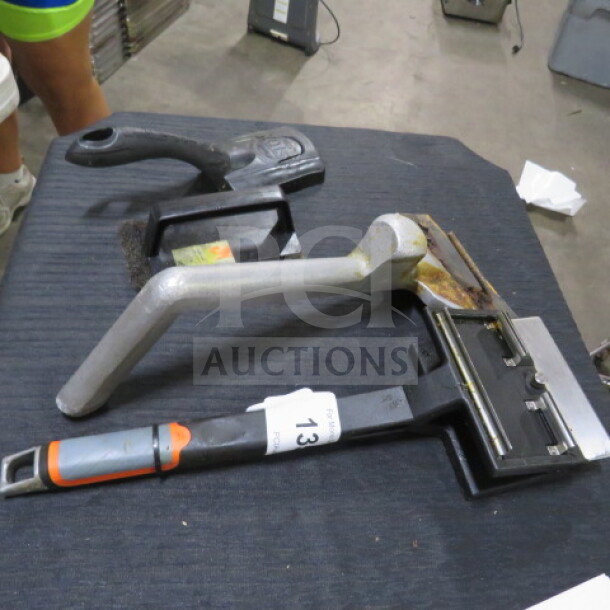 Lot of miscellaneous tools including a carpet kicker and two handheld tools on a table. Item tag labeled "13" visible.