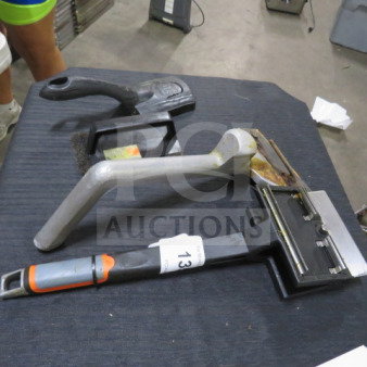 Lot of miscellaneous tools including a carpet kicker and two handheld tools on a table. Item tag labeled "13" visible.