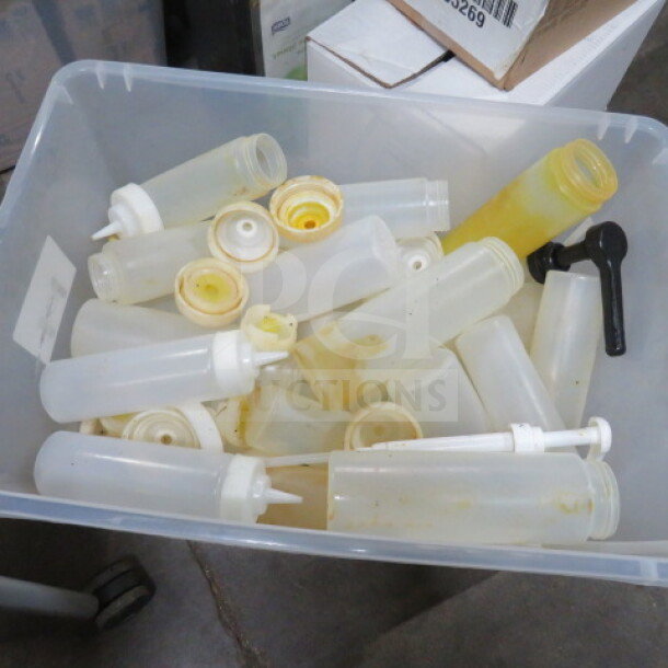 A collection of used squeeze bottles in a plastic bin, various sizes, white caps, signs of residue inside, suitable for bulk use.