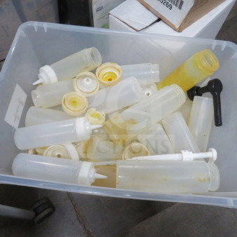 A collection of used squeeze bottles in a plastic bin, various sizes, white caps, signs of residue inside, suitable for bulk use.