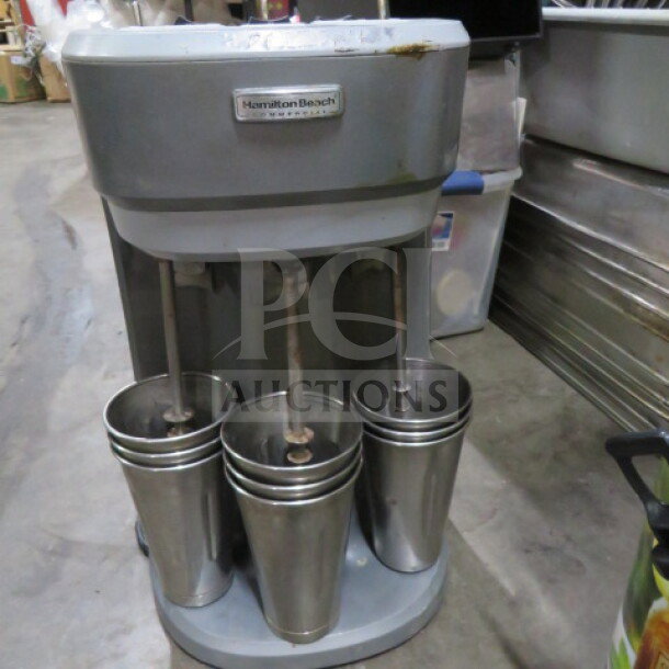 Hamilton Beach 3 Head Drink Mixer with 6 stainless steel mixing glasses, used condition, visible brand logo on the front.