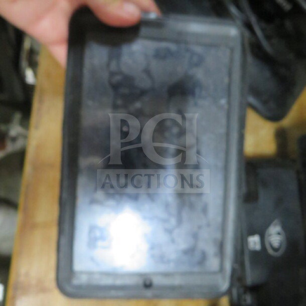 A tablet in a rugged black case, screen slightly smudged, no cords included. Condition appears to be used.