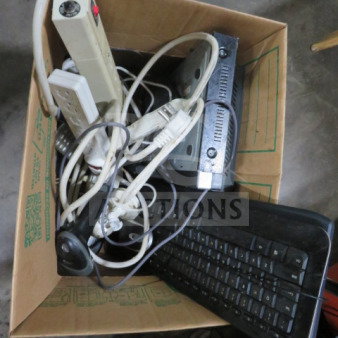 One lot of miscellaneous electronics in a cardboard box, including power strips, cables, a keyboard, and other misc items.