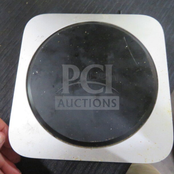 Mac Mini, silver, visible wear and dust on the bottom. Circular black base with faint markings. Good for parts or repair.